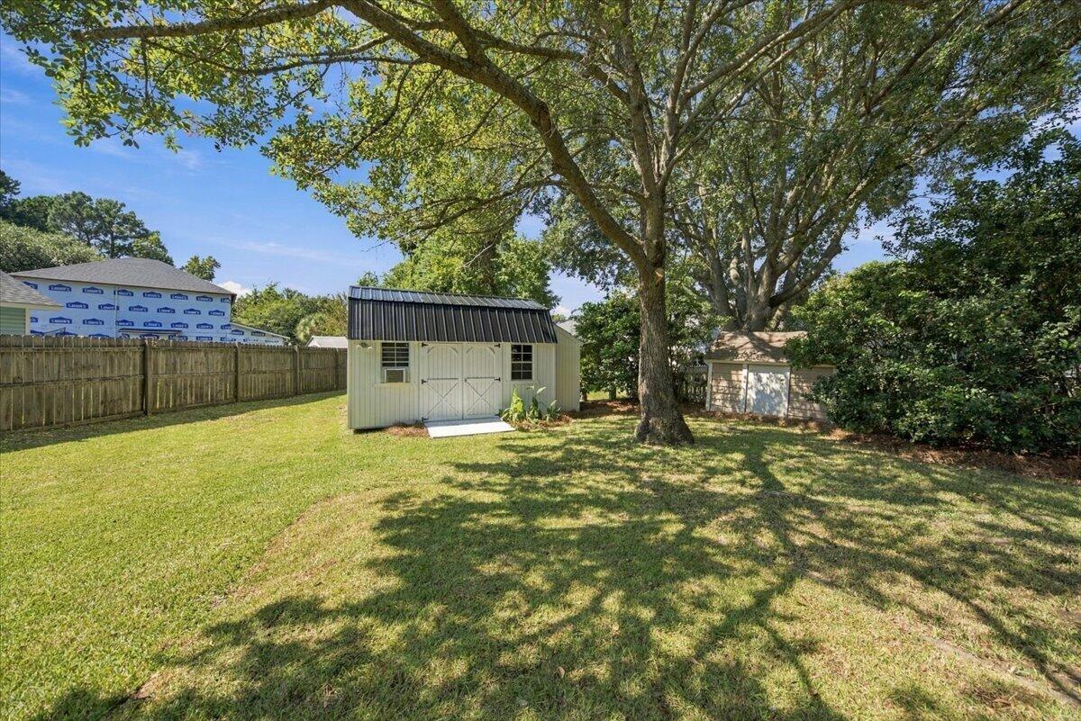Fenced backyard with a broad lawn, mature shade trees, and a light-colored storage shed.