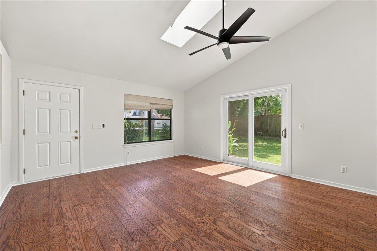 Empty room with wood flooring, a skylight, and sliding glass doors overlooking the backyard.