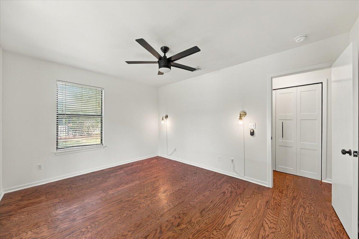Empty bedroom with hardwood floors, a ceiling fan, window blinds, and double closet doors.