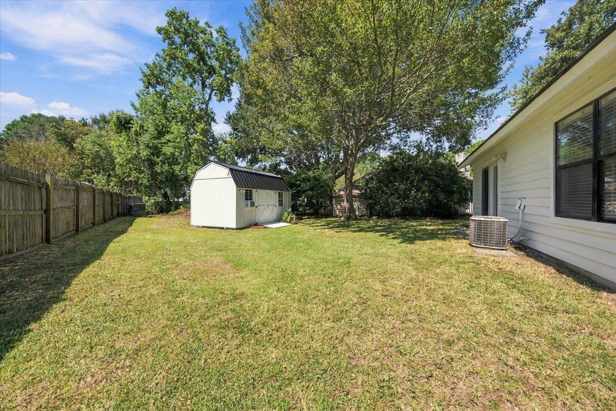 Backyard with a grassy lawn, white storage shed, mature trees, and wooden privacy fence.