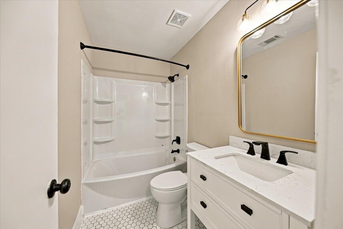 Bathroom with a white tub and shower, hexagonal tile floor, and white vanity with a gold-framed mirror.