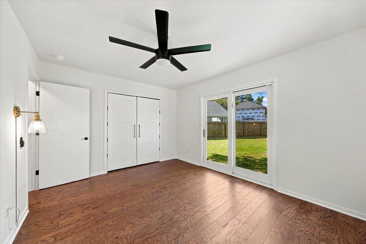Vacant bedroom with hardwood floors, double closets, and sliding doors to a fenced backyard.