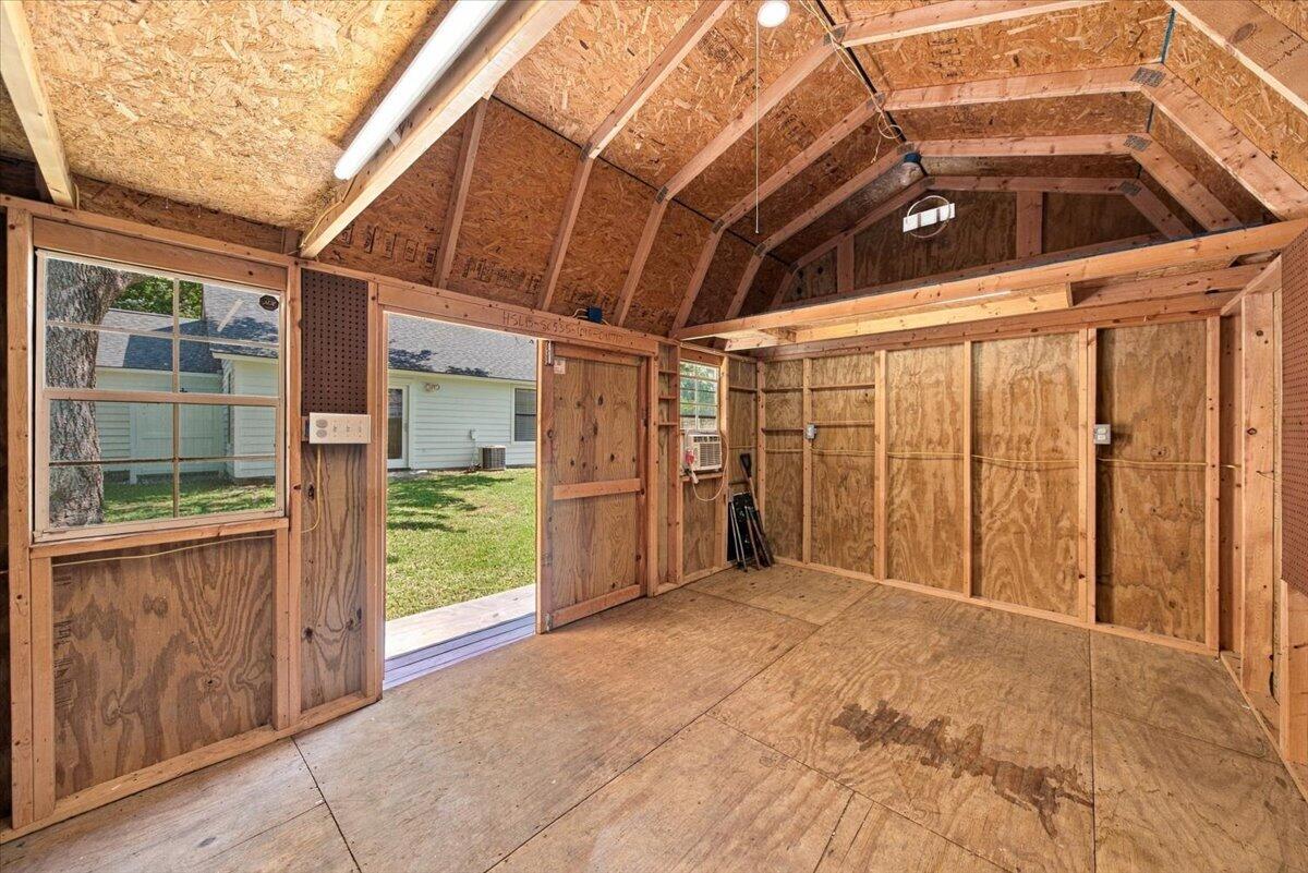 Empty wooden shed interior with exposed framing, a small window, and an open doorway to the yard.