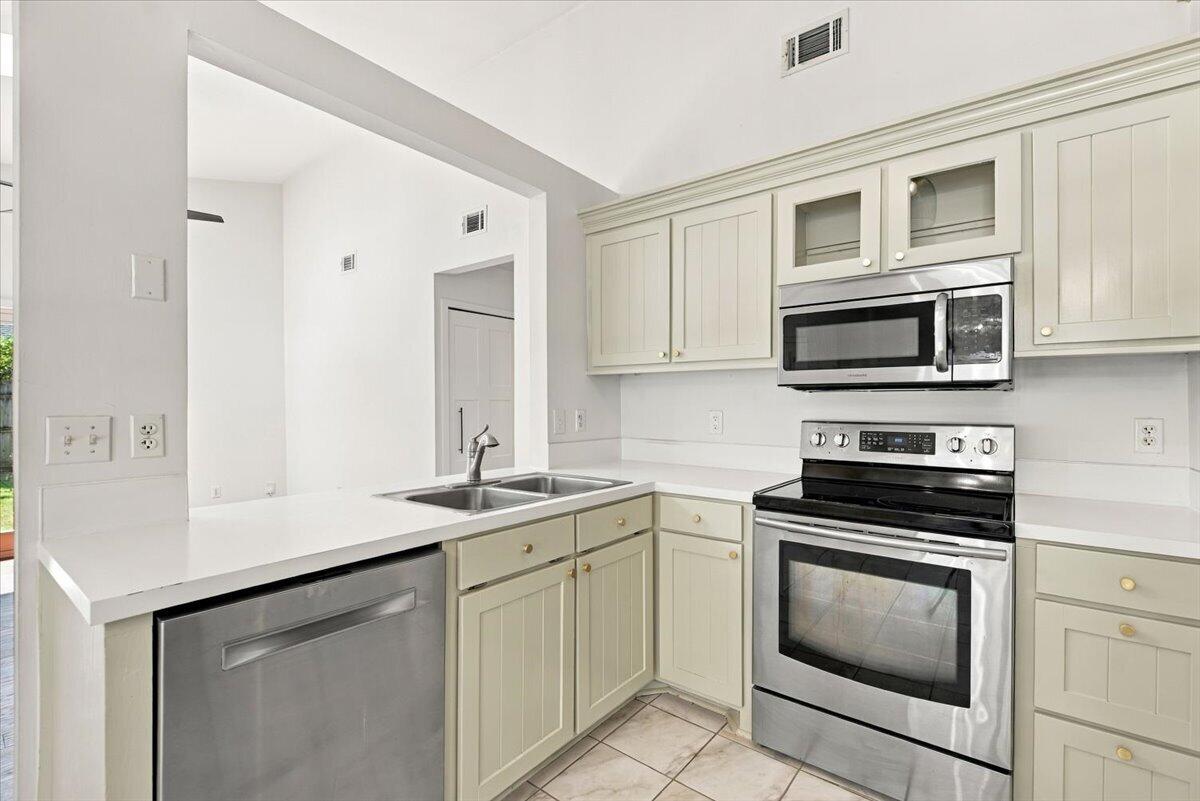 Kitchen with pale paneled cabinets, white counters, and stainless steel appliances.