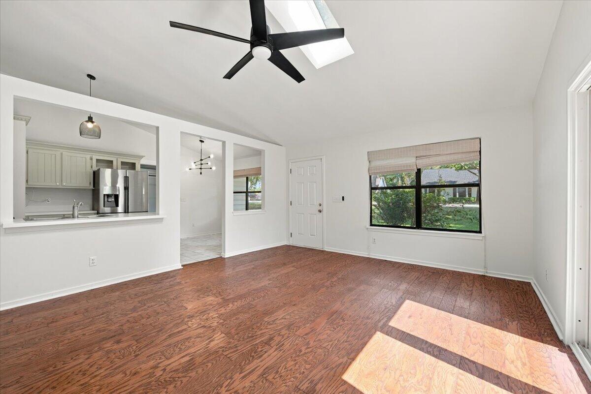 Vacant living room with reddish hardwood floors, black ceiling fan, and kitchen pass-through.