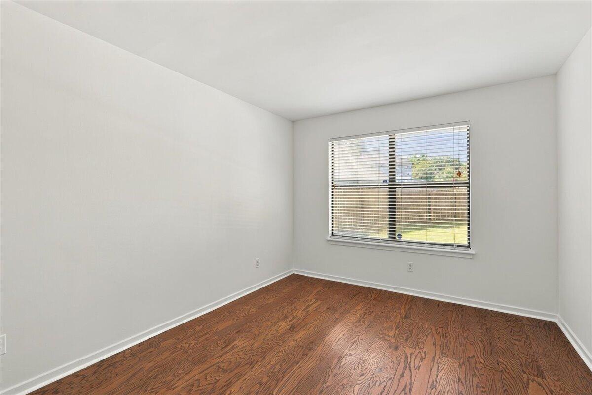 Empty bedroom with reddish-brown hardwood floors and a window overlooking a fenced yard.