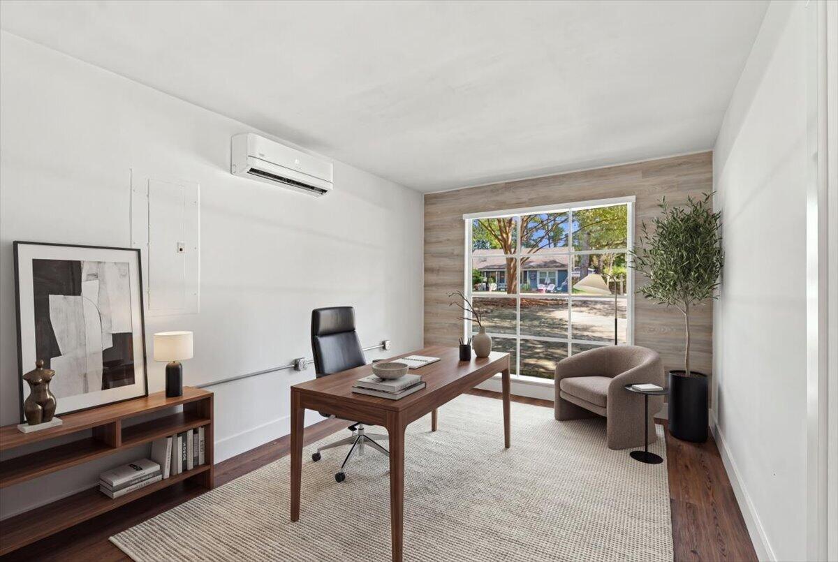 Staged home office with a wooden desk and black chair beside a large window.