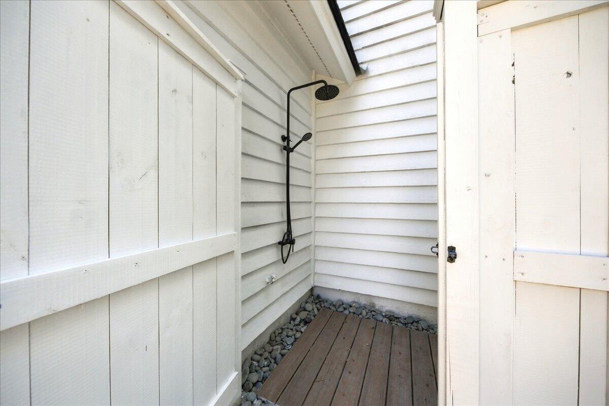 Outdoor shower with black fixtures, white siding, and a narrow wood-plank floor.