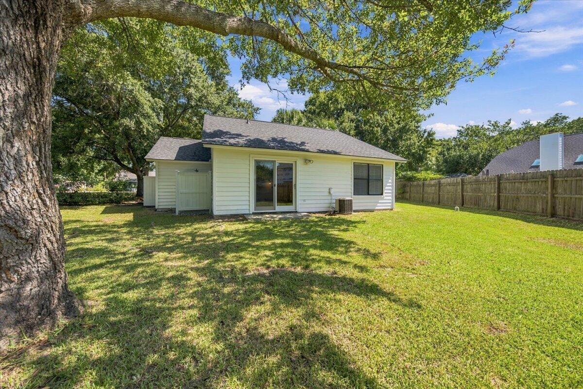 Rear of a light-colored home with sliding doors, a fenced lawn, and a large shade tree.