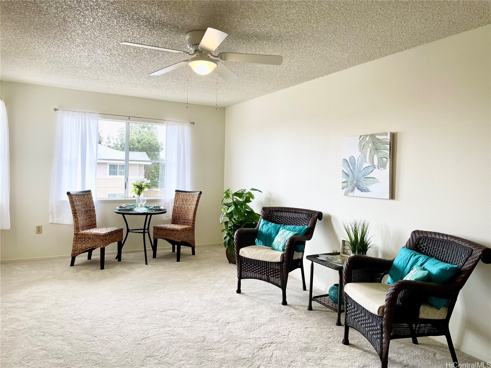 Living room with wicker armchairs, turquoise cushions, carpet, and a dining nook by the window.