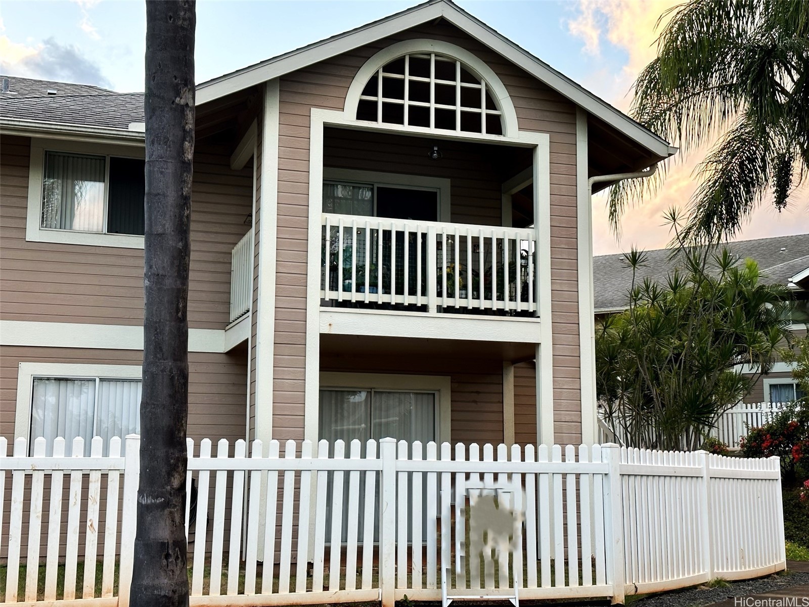 Two-story residence with a covered balcony, arched window, and white picket fence.