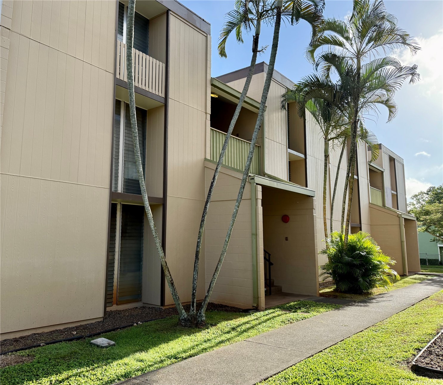 Beige multi-story residential building with balconies, palm trees, and a covered entrance.