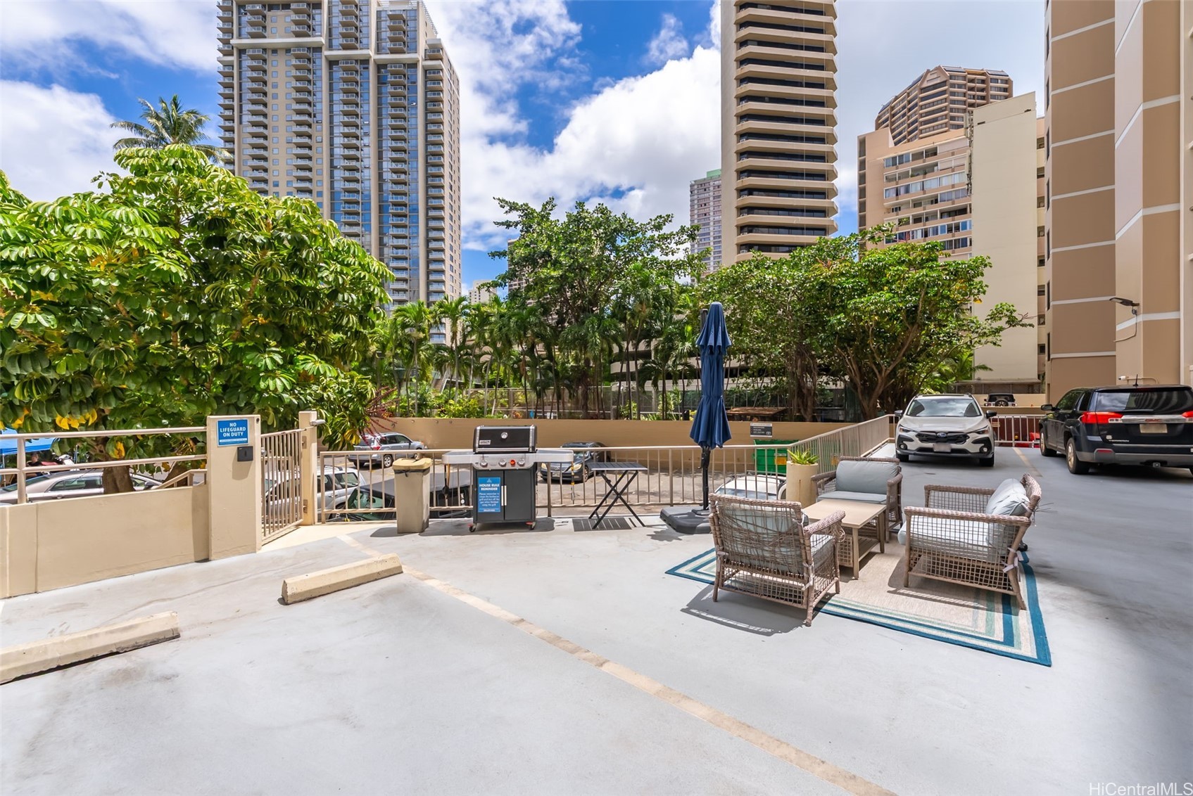 Condominium courtyard with a barbecue grill and wicker seating among high-rise buildings.