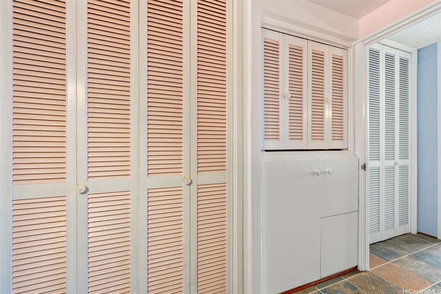 Built-in storage with pale pink louvered doors, white lower cabinets, and multicolored tile flooring.