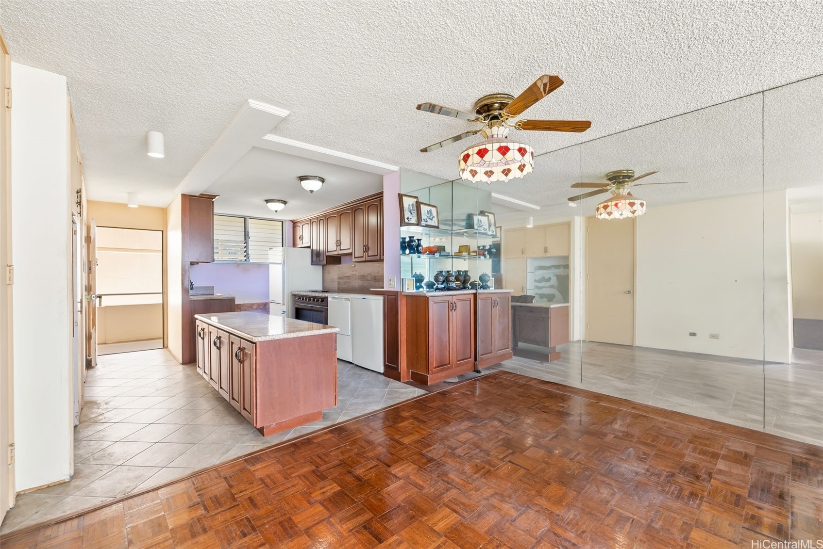Condo kitchen and dining area with a wood island, mirrored wall, parquet flooring, and stained-glass ceiling fan.