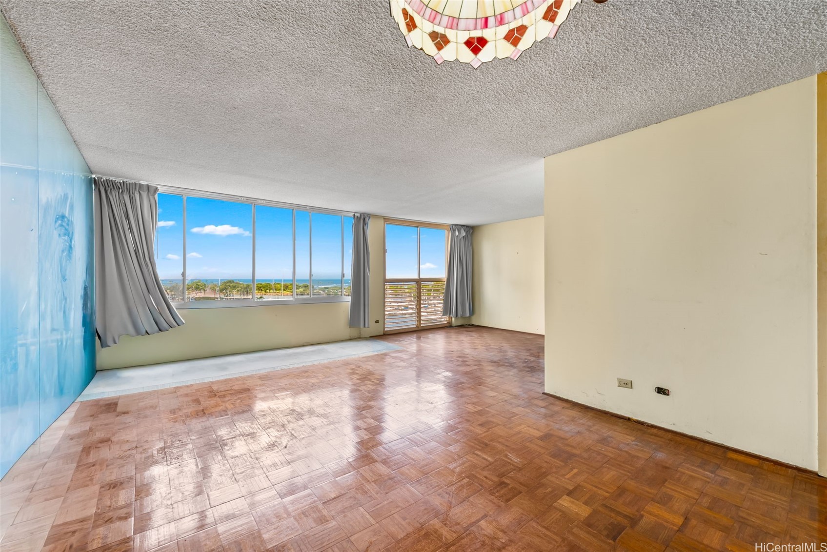 Empty living room with parquet floors, wide ocean-view windows, and a blue accent wall.