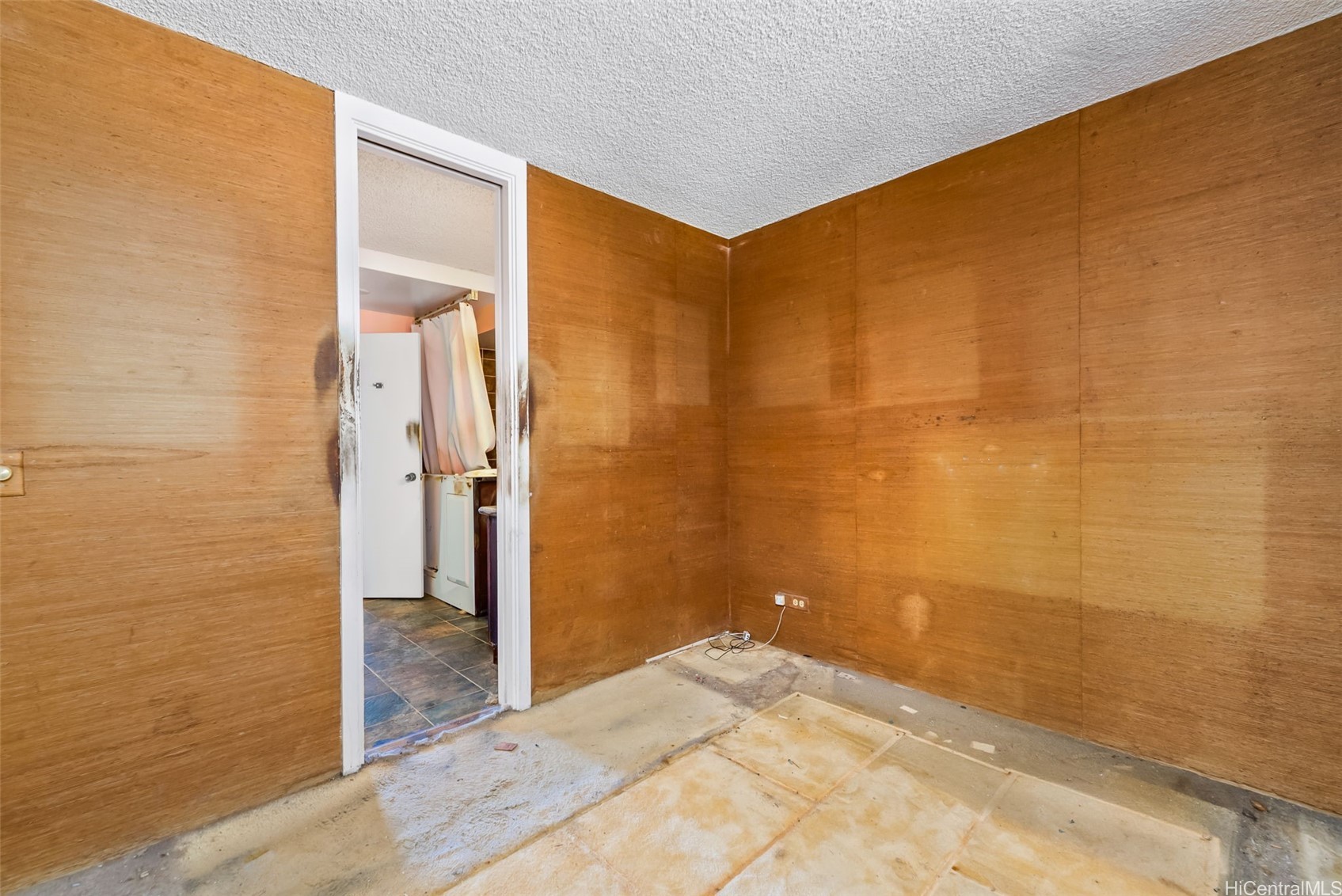 Unfinished room with wood-paneled walls, exposed flooring, and a doorway to a tiled area.