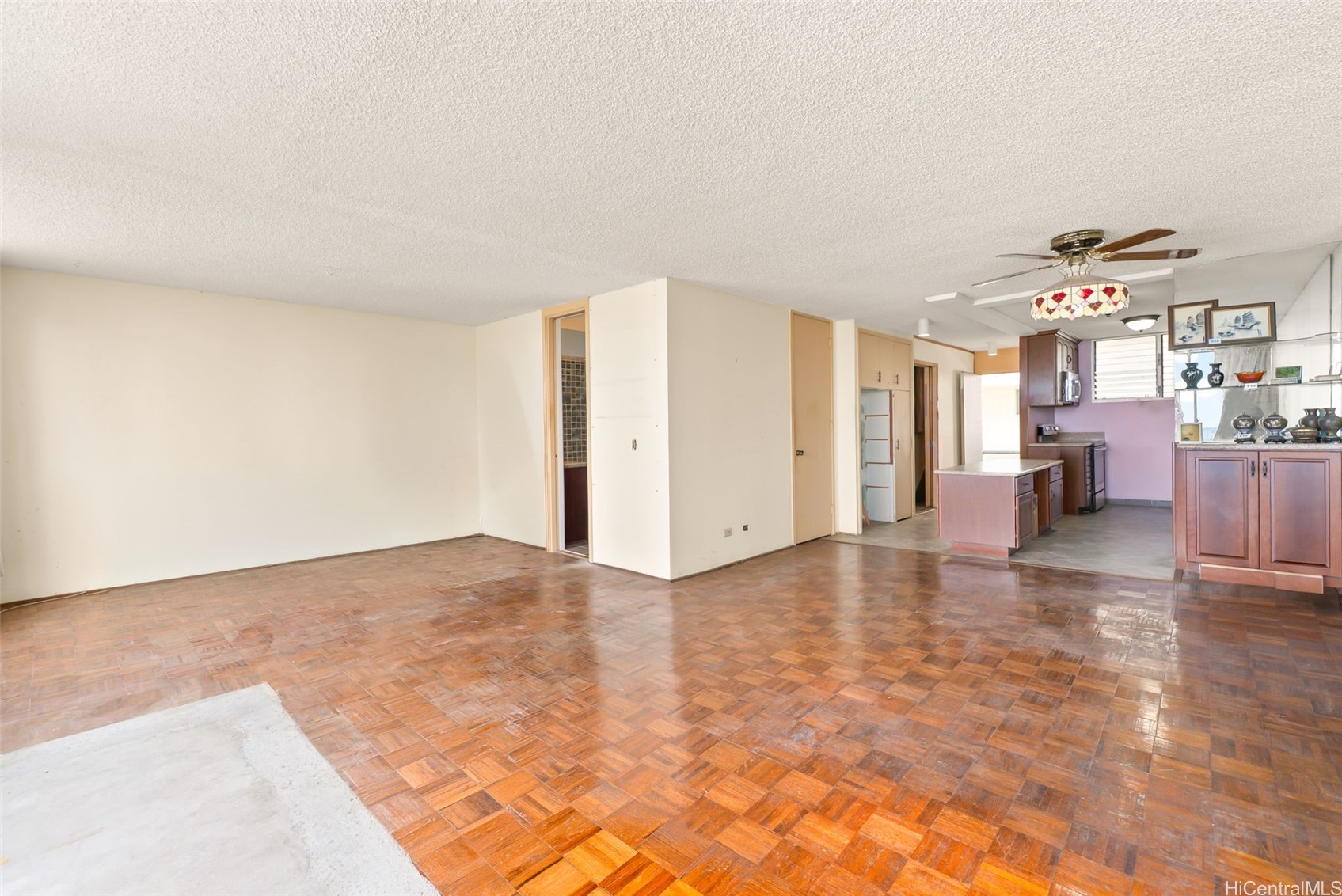 Vacant living room with parquet floors opening to a kitchen with dark wood cabinetry.