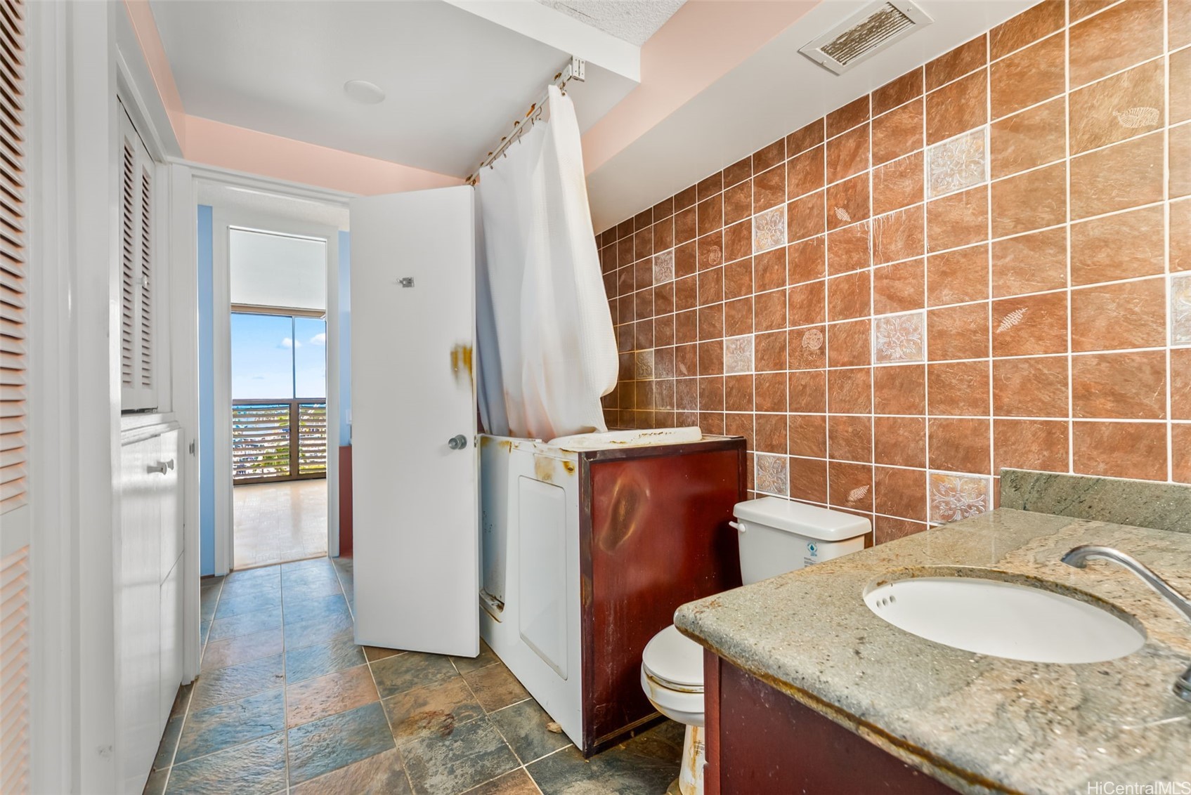 Bathroom with brown tiled walls, a granite vanity, and a curtained shower area.