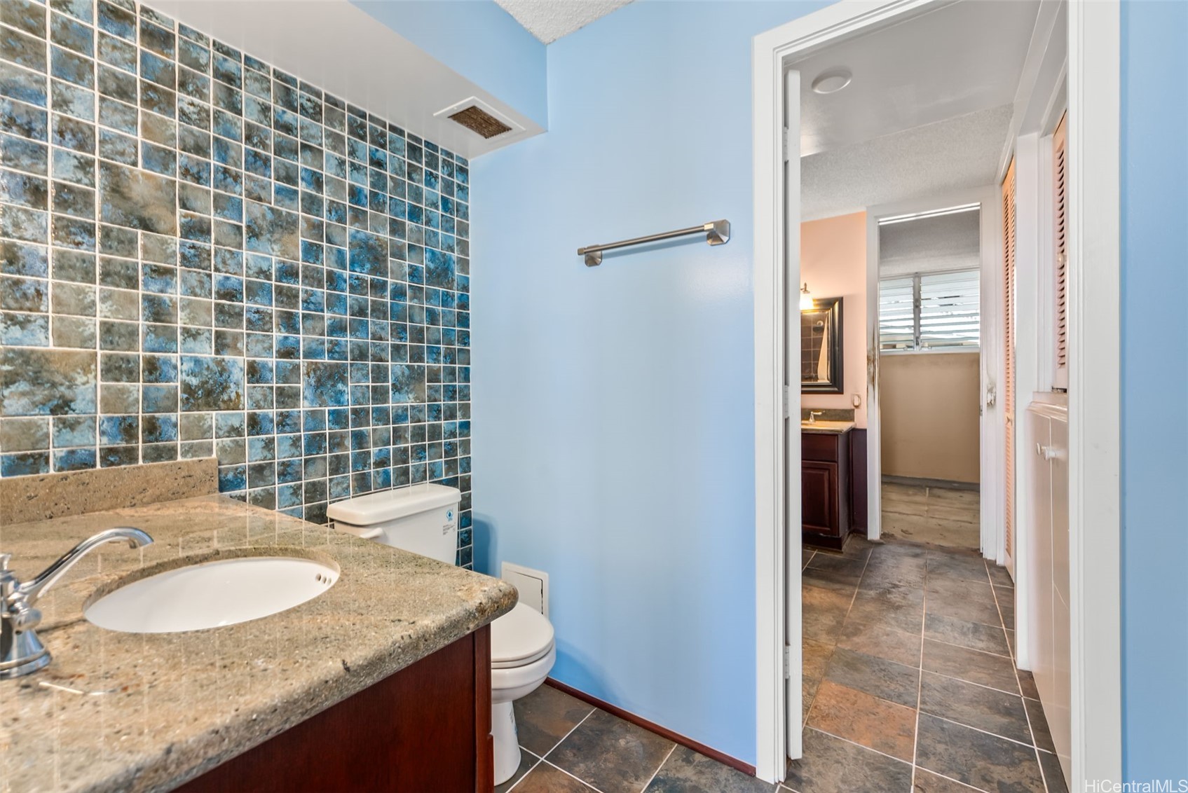 Bathroom with a granite vanity, blue mosaic tile wall, and doorway to an adjoining area.