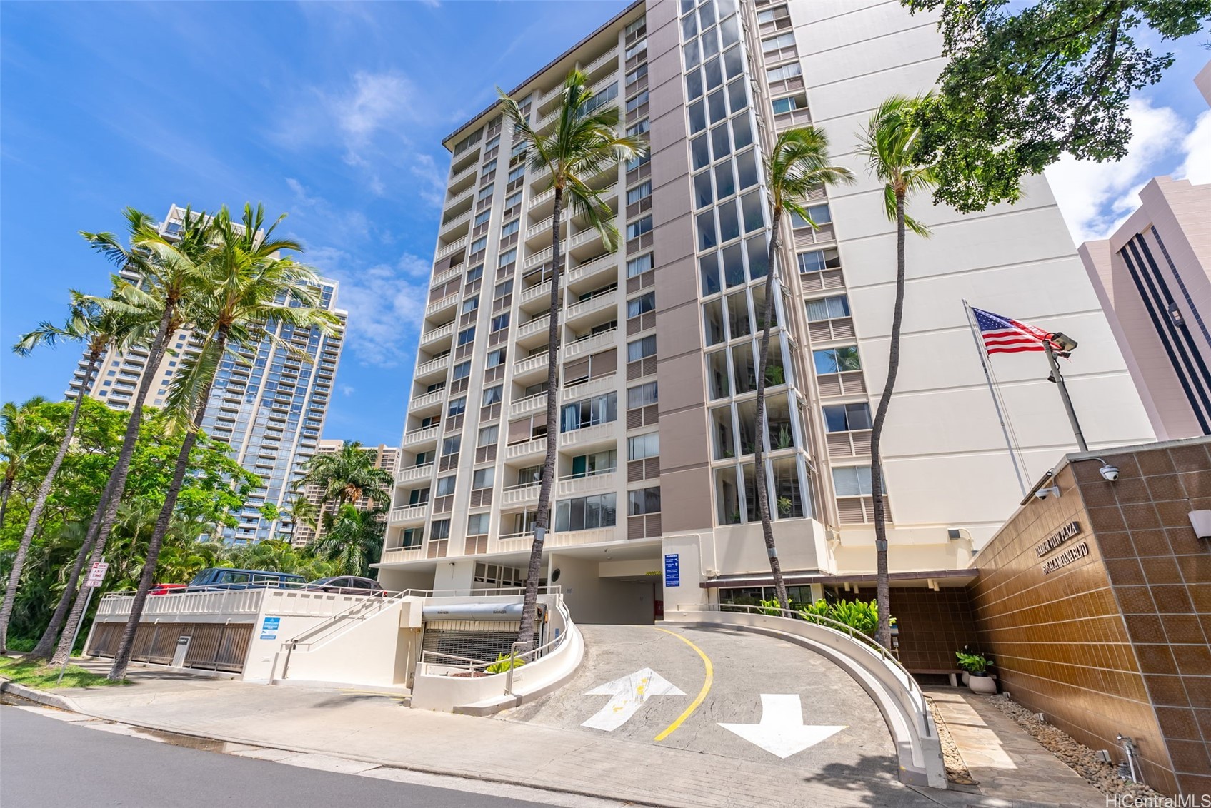 Condominium exterior with palm trees, balconies, and a curved entrance ramp.