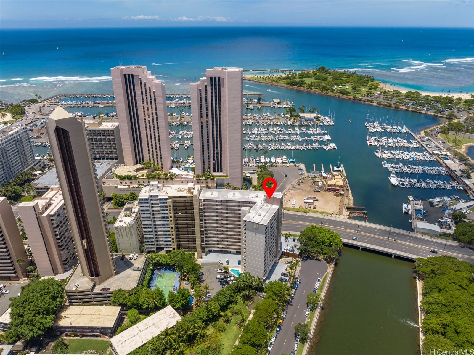 Aerial view of a condominium beside a marina, with the ocean and a red location marker.