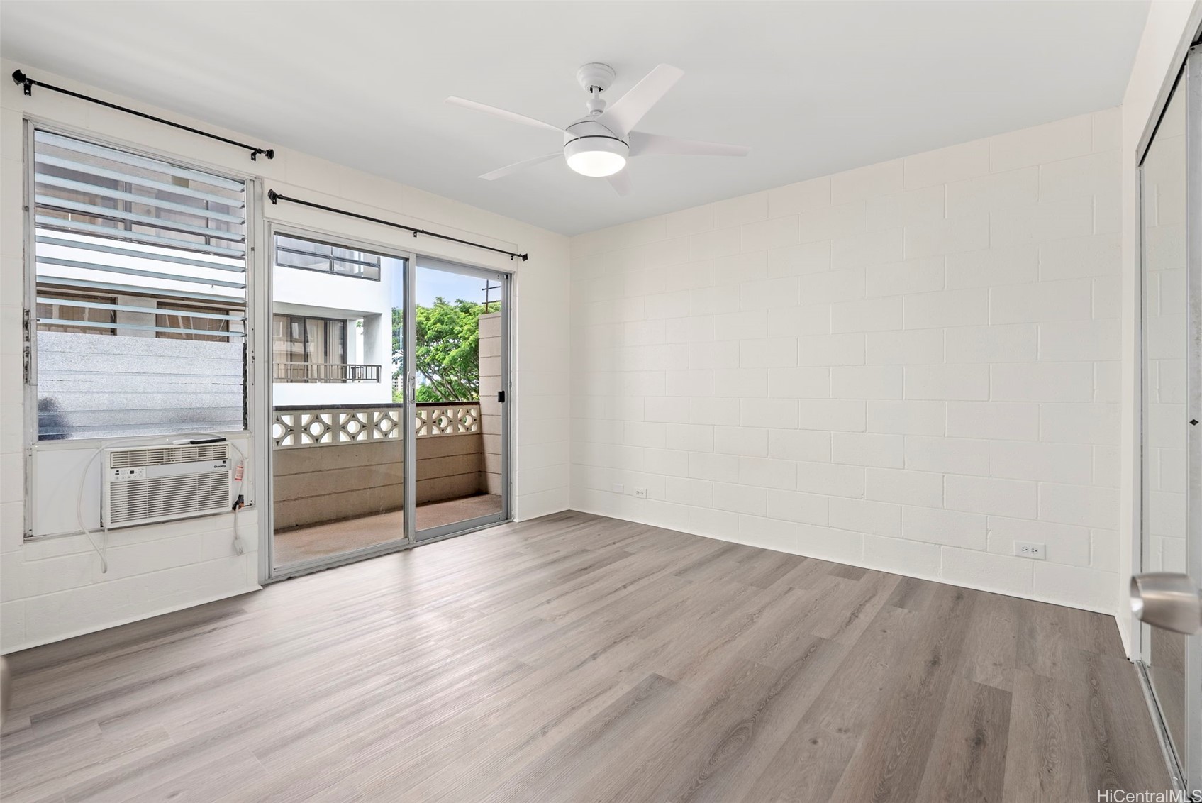 Vacant room with gray plank flooring, a ceiling fan, window air conditioner, and sliding doors to a balcony.