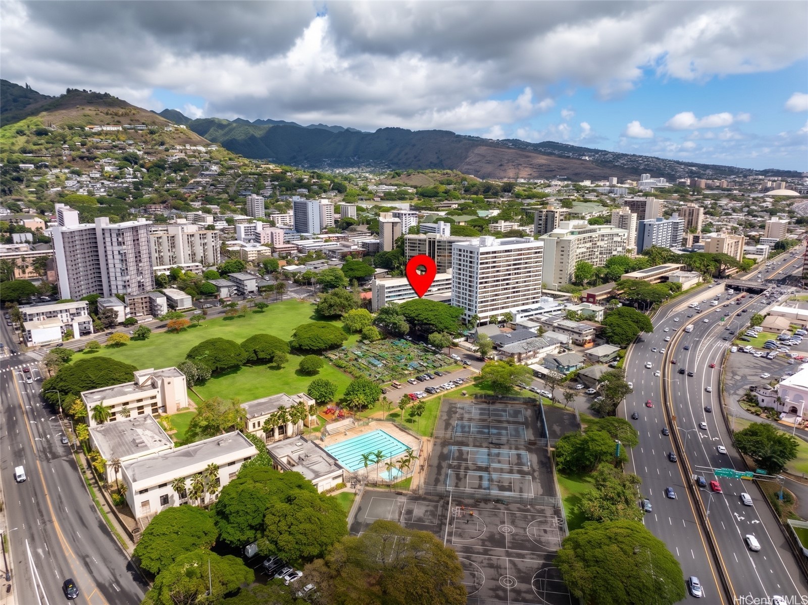Aerial view of the marked apartment building, with Honolulu, green mountains, a park, and tennis courts around it.