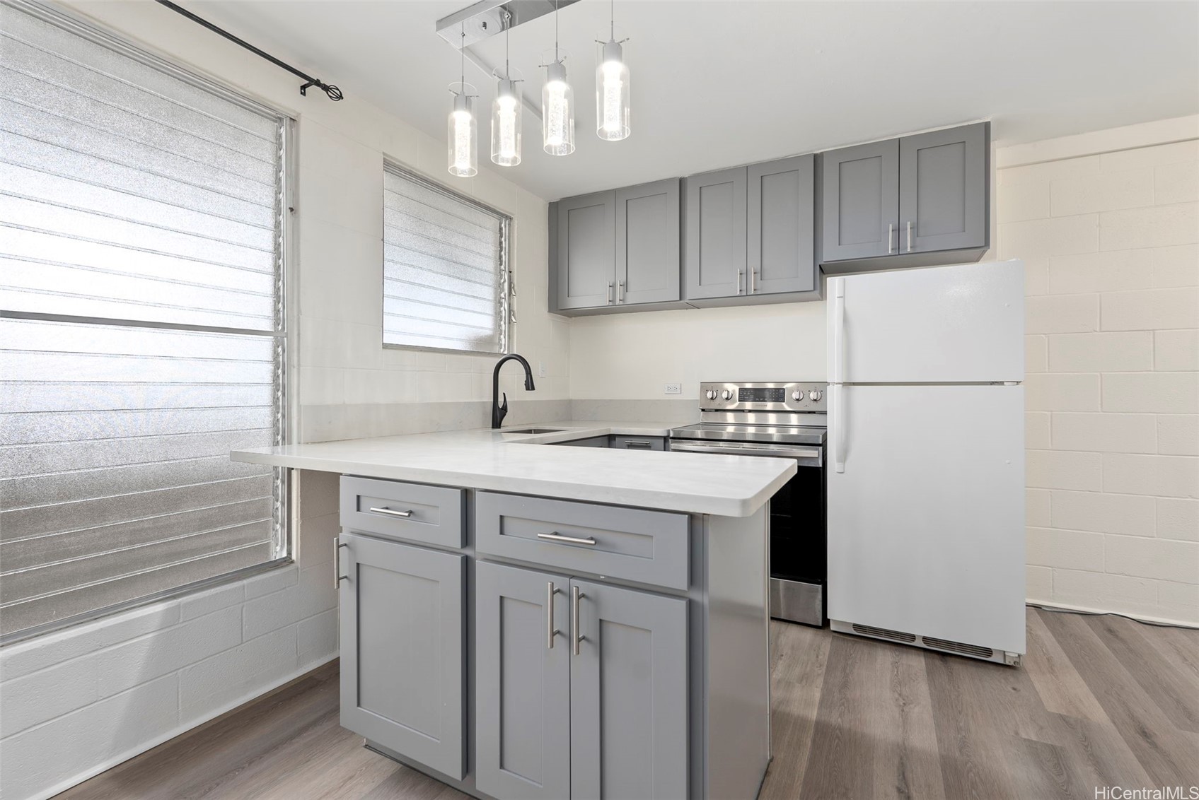 Kitchen with gray cabinets, a white island, stainless steel range, and louvered windows.