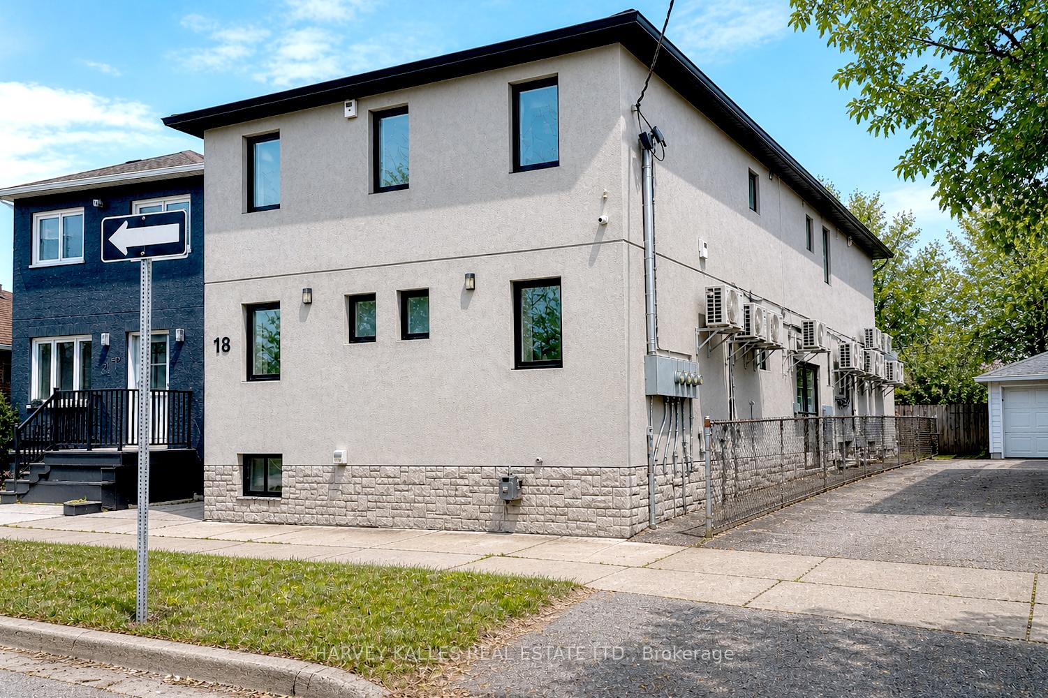 Two-storey commercial building numbered 18, with beige stucco walls and air conditioners along its fenced side.