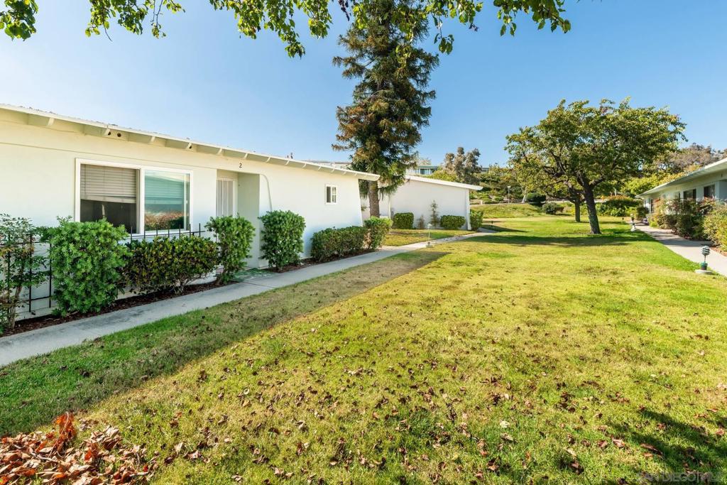 Single-story white residence beside a broad lawn, sidewalk, and mature trees.