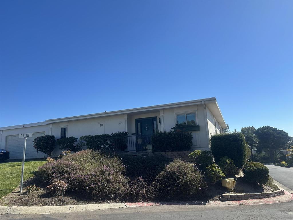 Single-story home with a blue front door, attached garage, and landscaped shrubs beside F Street.