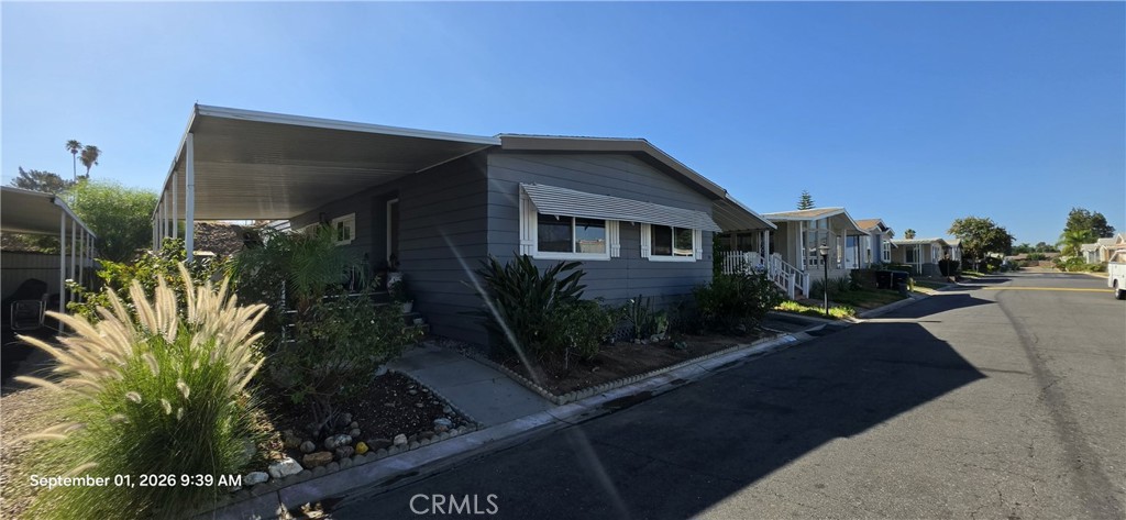 Blue-sided manufactured home with a covered carport and landscaped frontage in a residential community.