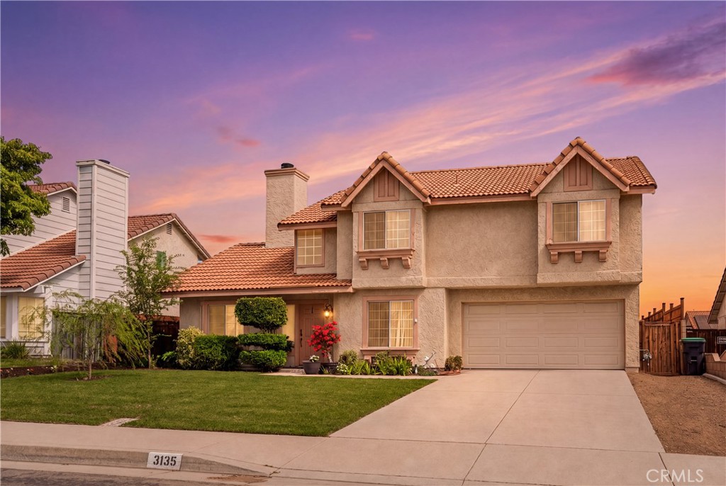 Two-story stucco home with terracotta tile roof and double garage beneath a colorful sunset sky.