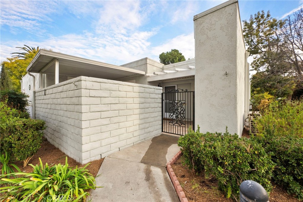 White stucco home with a walled courtyard, decorative gate, and shrub-lined walkway.
