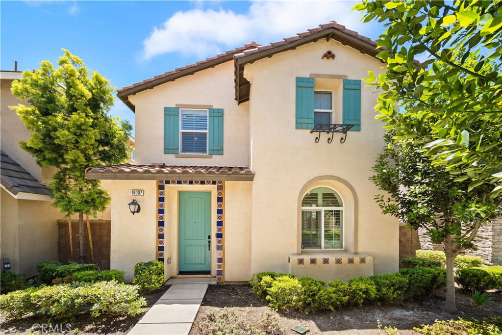 Two-story stucco home with a turquoise door, matching shutters, and colorful tile accents around the entrance.