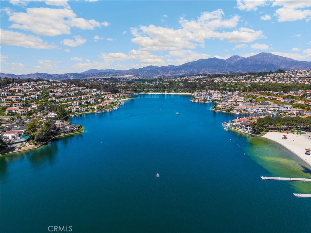 Aerial view of a blue lake bordered by homes, a sandy beach, and distant mountains.