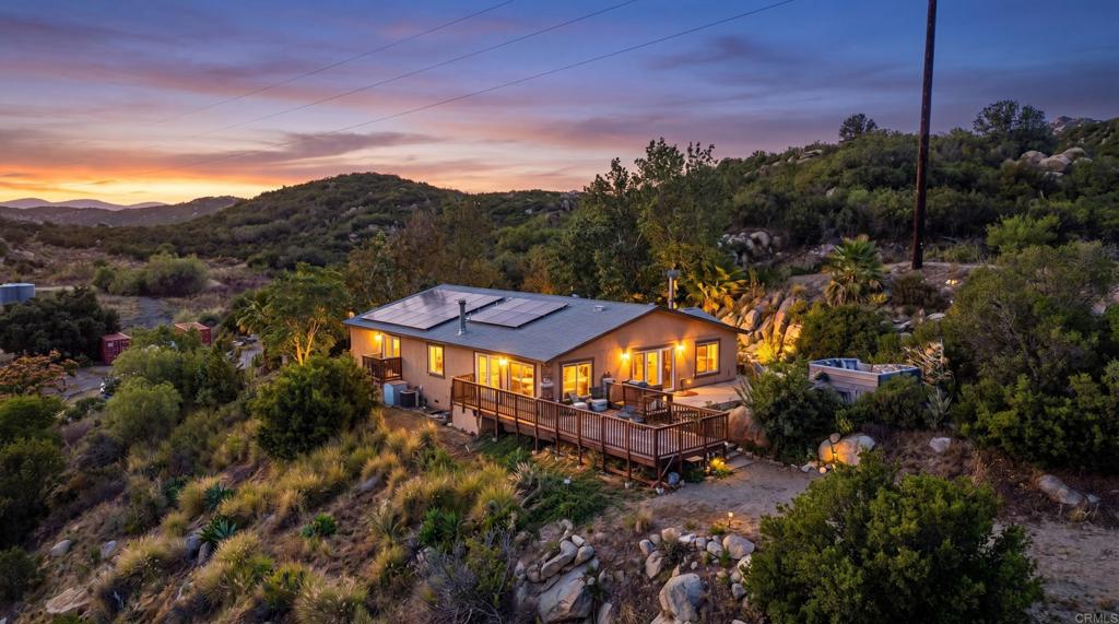 A hillside home with solar panels and a deck glowing at sunset.