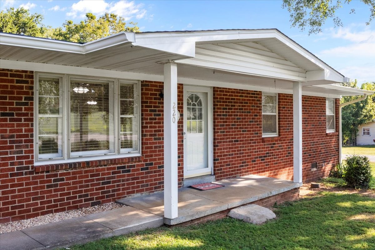 Red brick house with a broad white covered porch and glass-paneled front door.