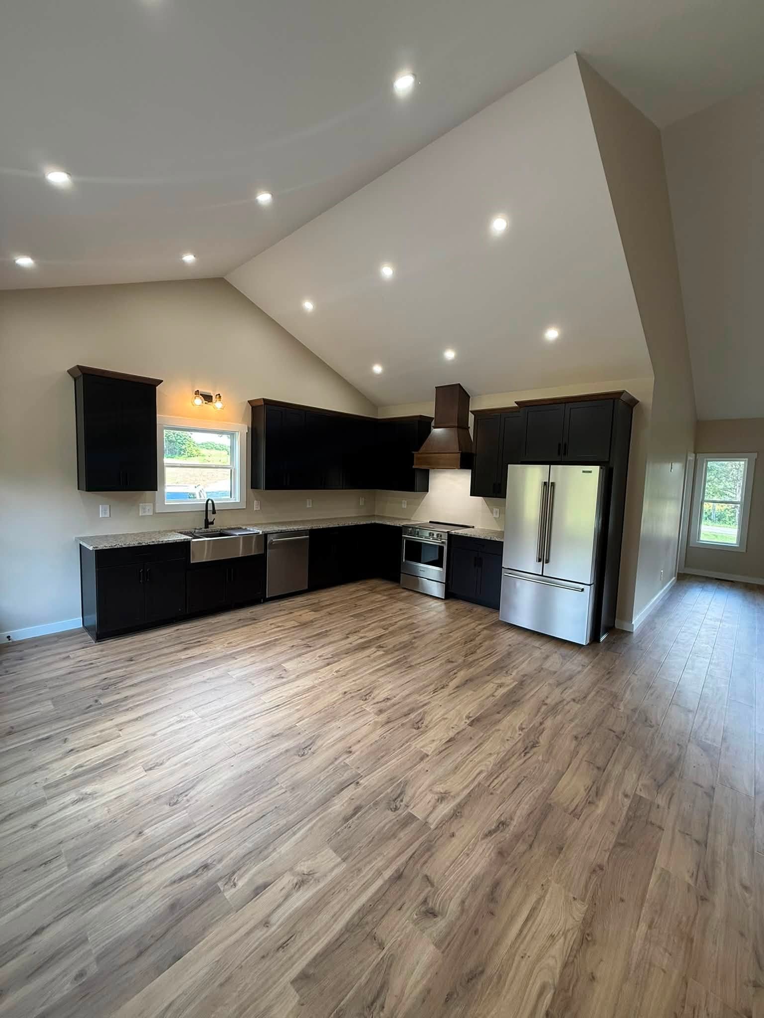 Kitchen with dark cabinets, stainless steel appliances, wood-look floors, and a high vaulted ceiling.