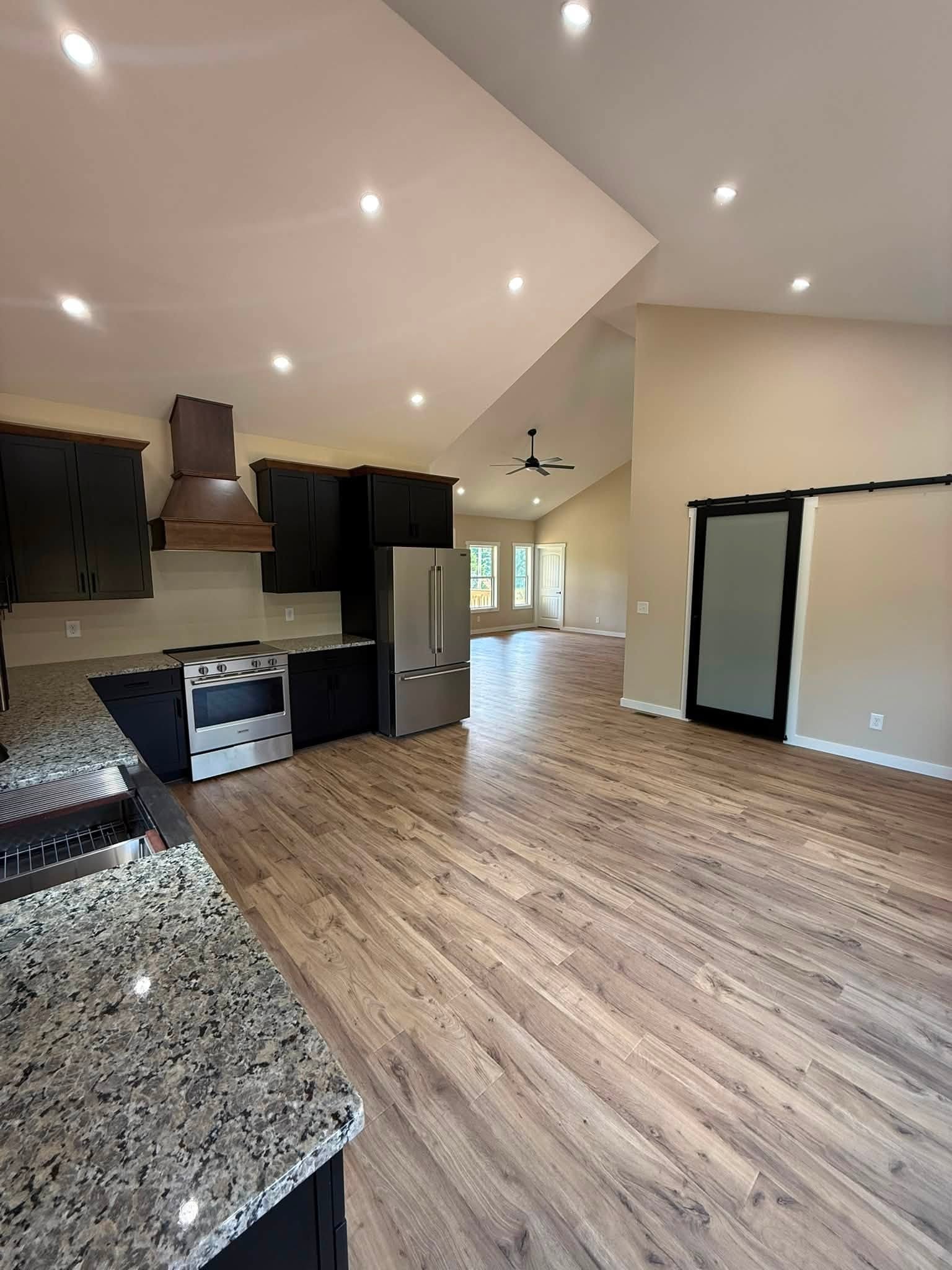 Open-plan kitchen with dark cabinets, granite counters, stainless steel appliances, and vaulted ceiling.