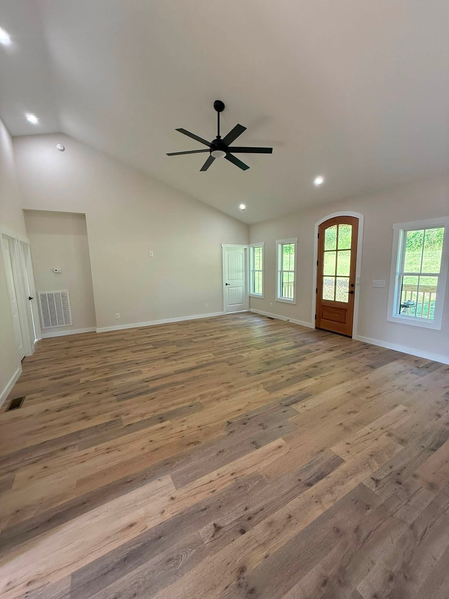Empty living room with wide-plank wood floors, a high ceiling, and a wood-framed glass door.