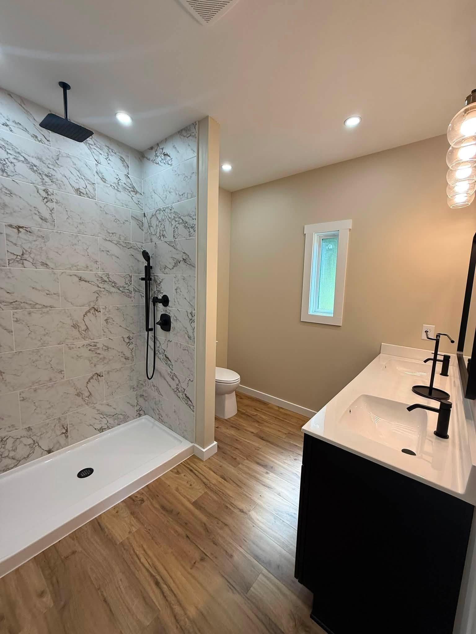 Bathroom with a marble-look tiled walk-in shower, black fixtures, and a black vanity with white sink.