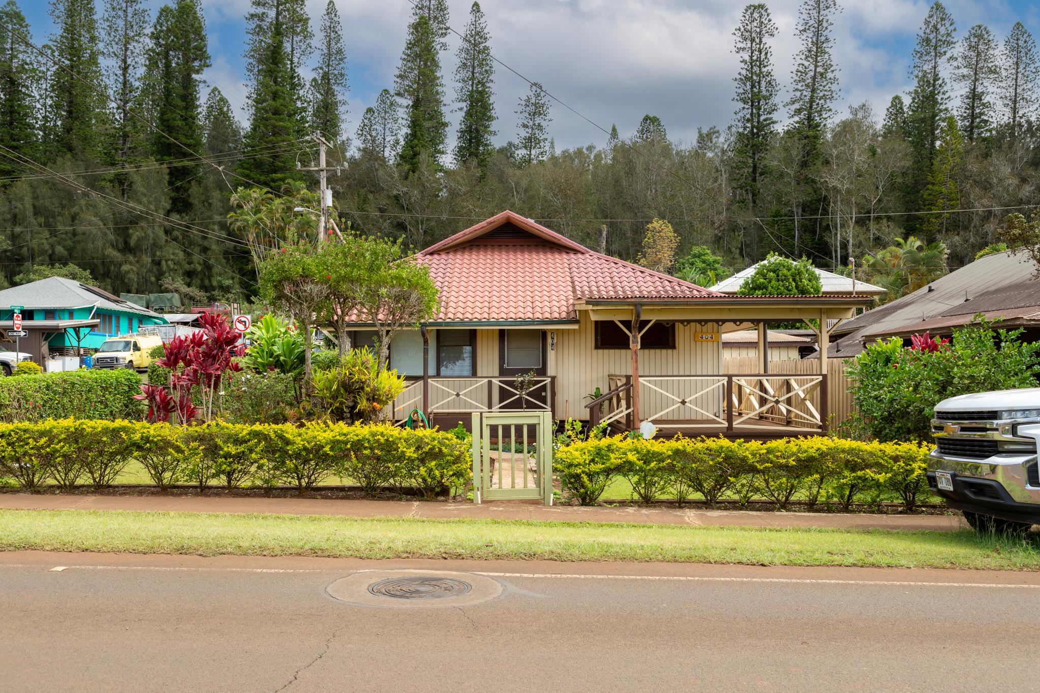 Single-story home with a reddish tile roof, covered porch, and colorful tropical landscaping.