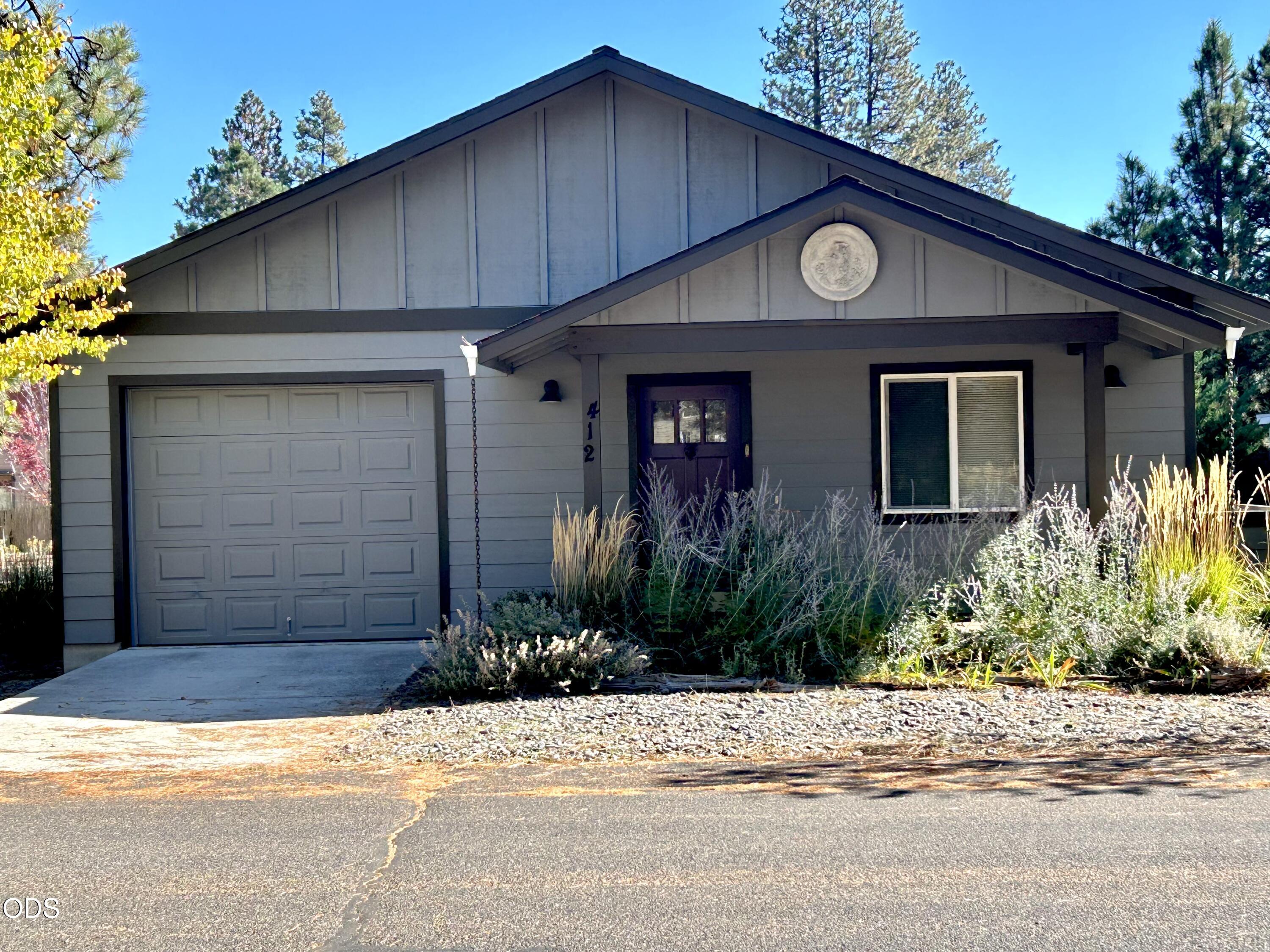 Gray single-story home with attached garage, purple front door, and ornamental grasses.
