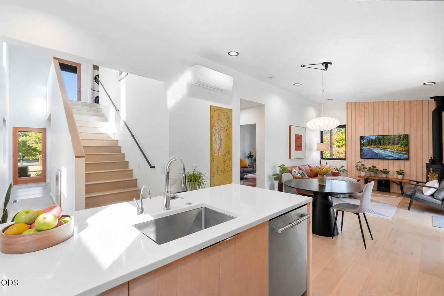Open-plan kitchen with a white island, wood cabinetry, staircase, and adjoining furnished living room.