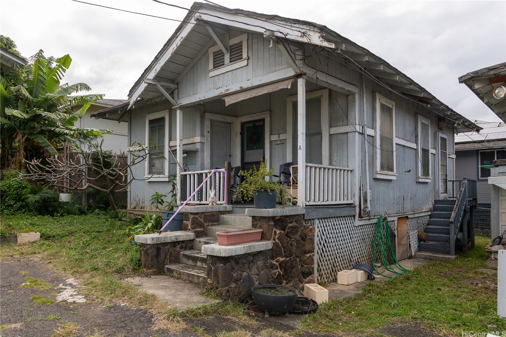 Weathered gray wooden house with a covered porch, stone steps, and overgrown yard.