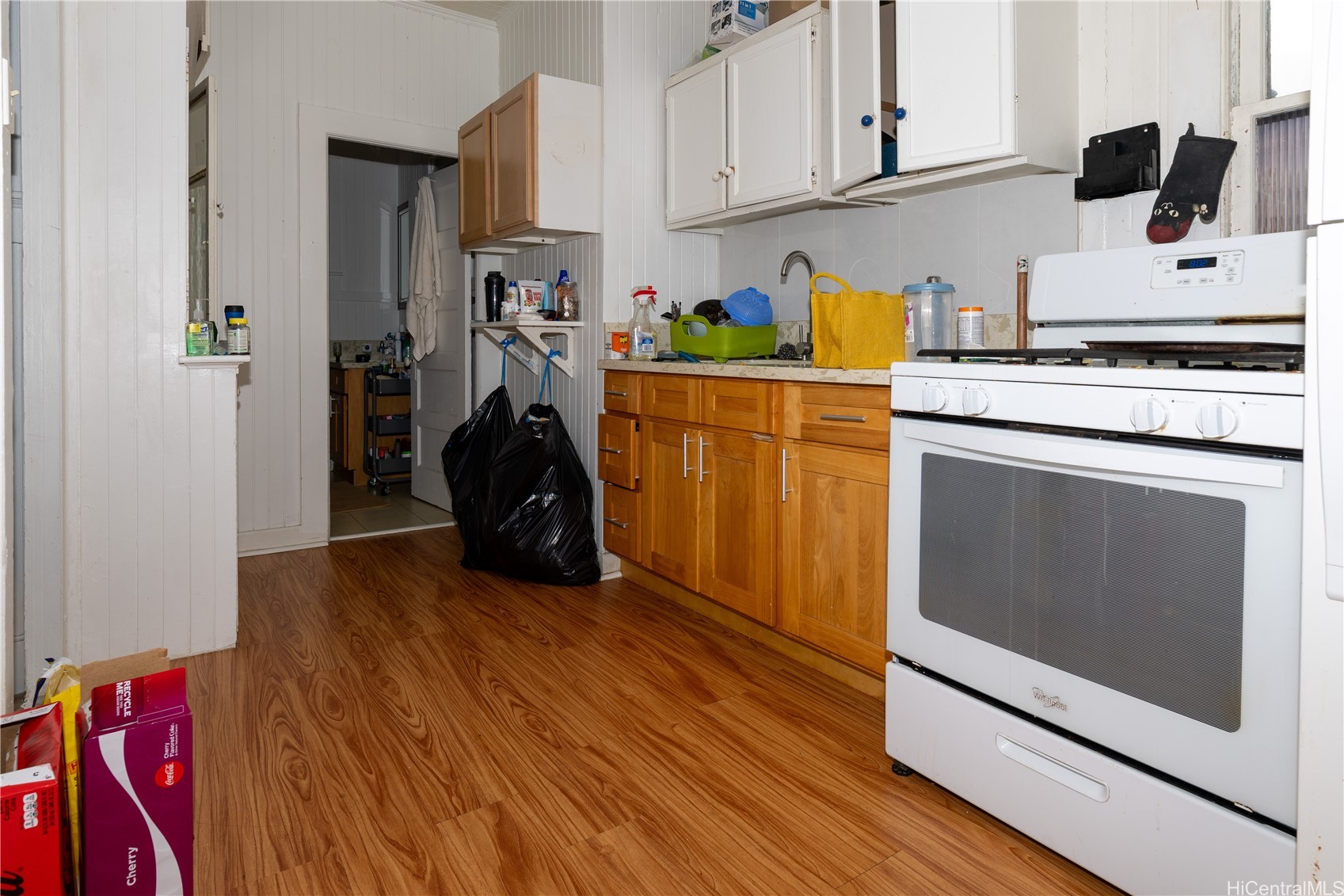 Kitchen with white cabinets, a gas range, honey-colored lower cabinets, and wood-look flooring.