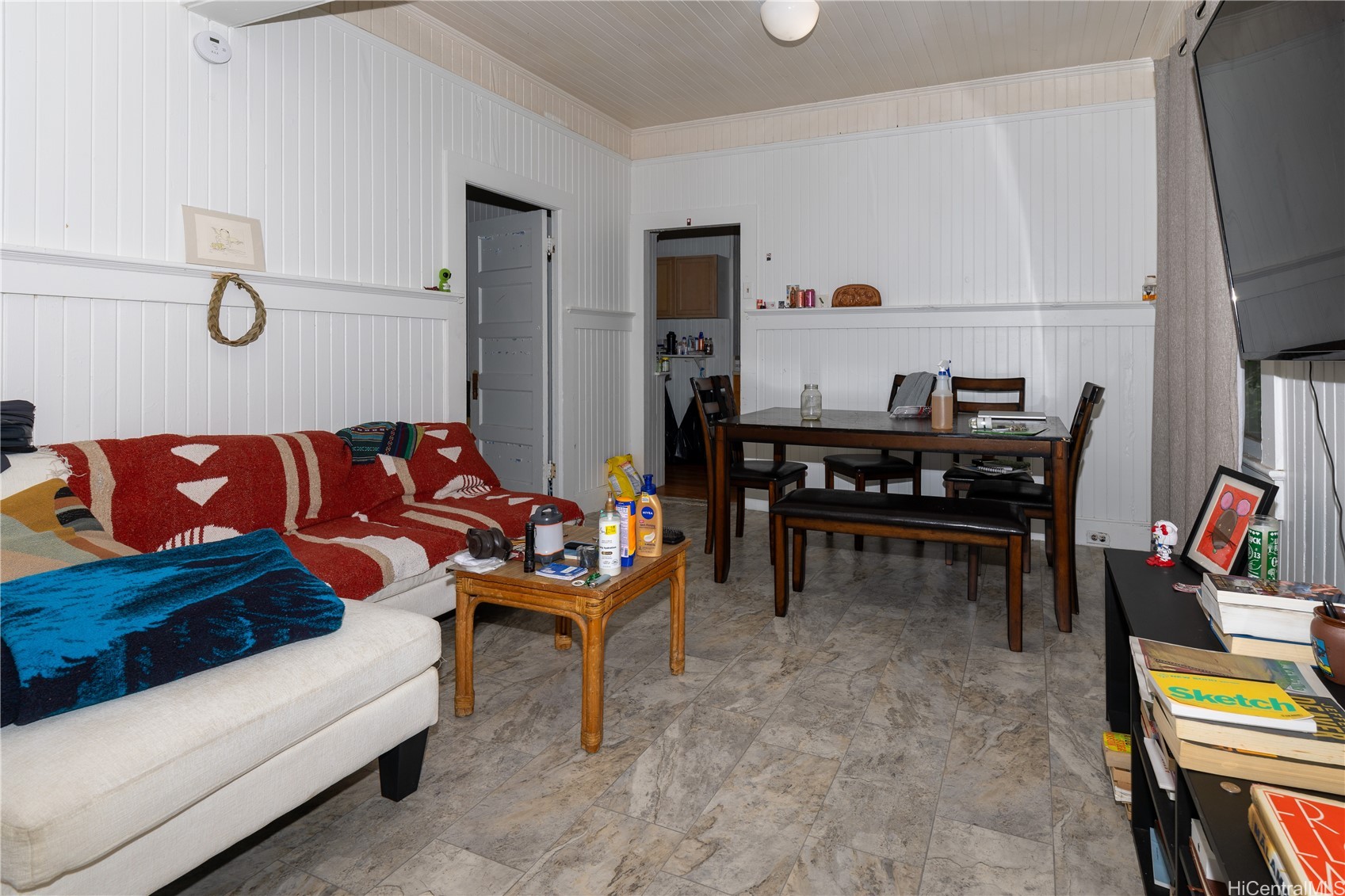 Living and dining room with a red patterned sofa, dark wood table, and white paneled walls.