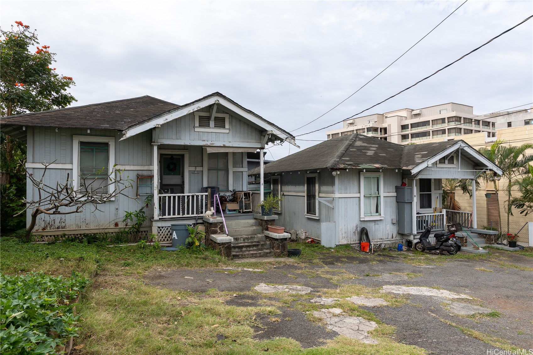 Two weathered gray cottages with front porches beside modern multi-story buildings.